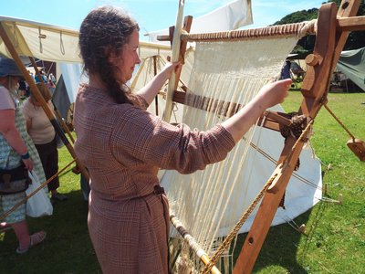 Reenactor beating cloth on a vertical weighted loom
